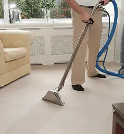 Professional carpet cleaner using a hot-water extraction wand and hose machine in a living room in Cedar Rapids, IA.