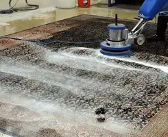 Professional rug cleaning with a rotary floor machine and shampoo foam, deep-cleaning an area rug, in Cedar Rapids, IA.
