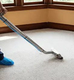 Steam carpet cleaning technician using a hot-water extraction wand on a residential carpet, wearing blue protective shoe covers Cedar Rapids, IA.