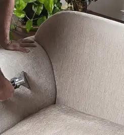 Professional upholstery cleaner deep-cleaning a fabric sofa with a handheld extraction tool and hose Cedar Rapids, IA.