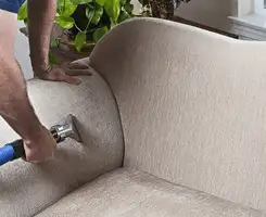 Professional upholstery cleaner deep-cleaning a fabric sofa with a handheld extraction tool and hose in Cedar Rapids, IA.